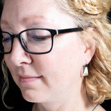 Woman wearing triangle-shaped sterling silver earrings stamped with flowers from Capulin Creations