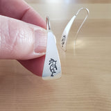 Woman Holding Triangle-Shaped Dangle Earrings in Sterling Silver Stamped with Kokopelli