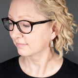 Woman Wearing Triangle-Shaped Dangle Earrings in Sterling Silver Stamped with Kokopelli