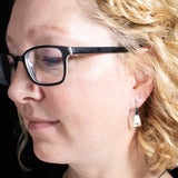 Woman Wearing Triangle-Shaped Dangle Earrings in Sterling Silver Stamped with Sprouts