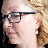 Woman wearing triangle-shaped sterling silver earrings stamped with square spirals from Capulin Creations