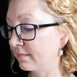 Woman Wearing Triangle-Shaped Dangle Earrings in Sterling Silver Stamped with Two Hearts
