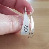 Woman Holding Triangle-Shaped Dangle Earrings in Sterling Silver Stamped with Kokopelli