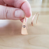 Woman Holding Triangle-Shaped Dangle Earrings in Copper Stamped with Large Spirals
