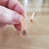 Woman Holding Triangle-Shaped Dangle Earrings in Copper Stamped with Large Spirals