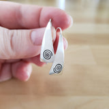 Woman Holding Triangle-Shaped Dangle Earrings in Sterling Silver Stamped with Large Spirals