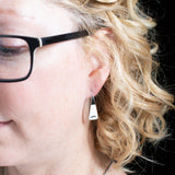 Woman wearing triangle-shaped sterling silver earrings stamped with sunrays from Capulin Creations