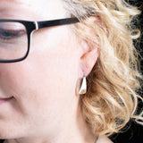 Woman wearing triangle-shaped sterling silver earrings stamped with triple spiral from Capulin Creations